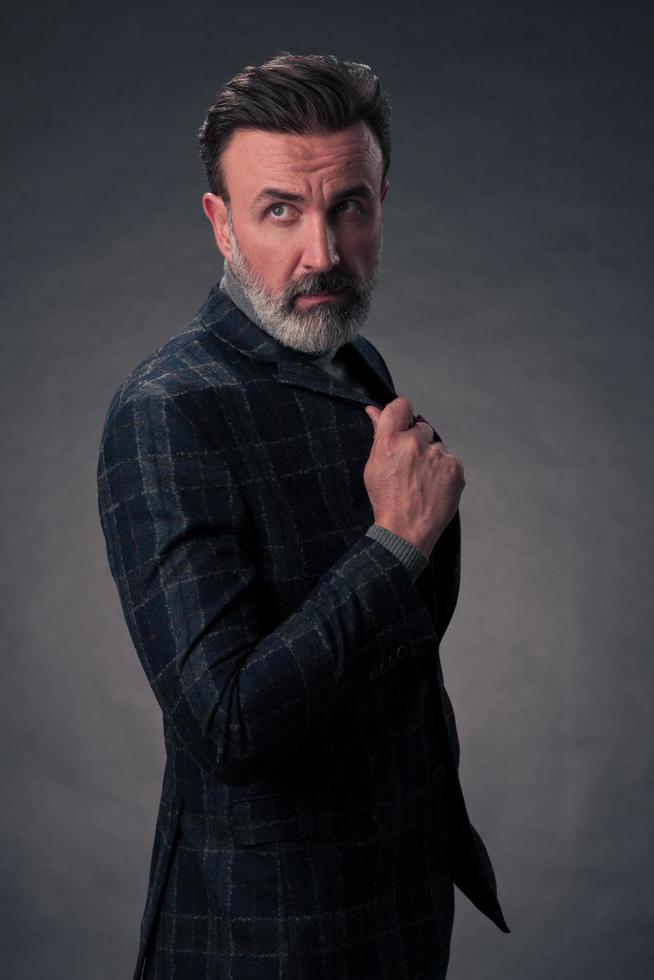 Portrait of a stylish elegant senior businessman with a beard and casual business clothes in photo studio isolated on dark background gesturing with hands