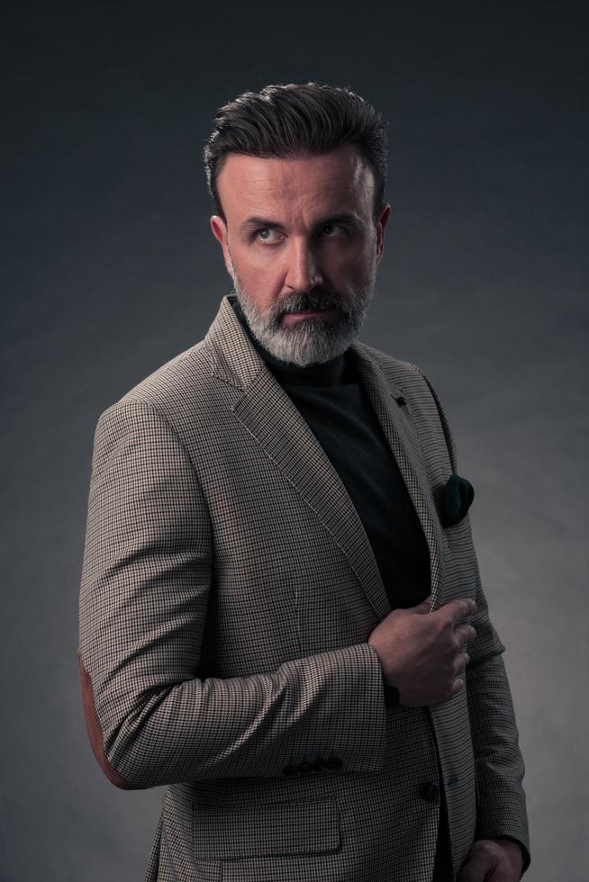 Portrait of a stylish elegant senior businessman with a beard and casual business clothes in photo studio isolated on dark background gesturing with hands