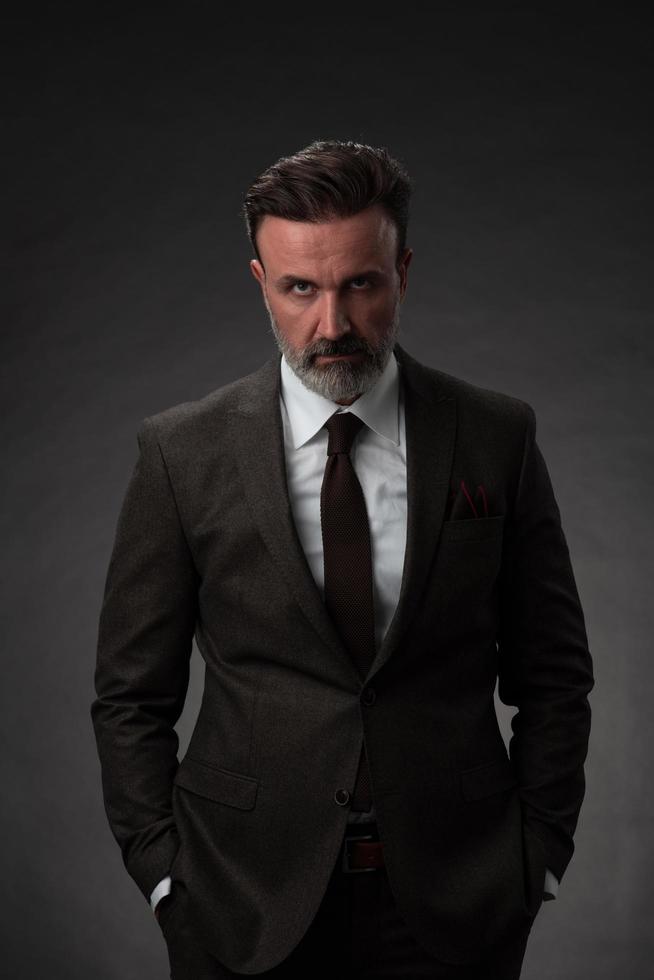 Portrait of a stylish elegant senior businessman with a beard and casual business clothes in photo studio isolated on dark background gesturing with hands