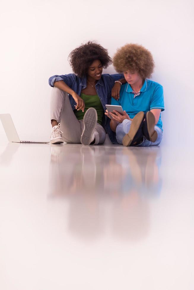 pareja multiétnica sentada en el suelo con una laptop y una tableta foto