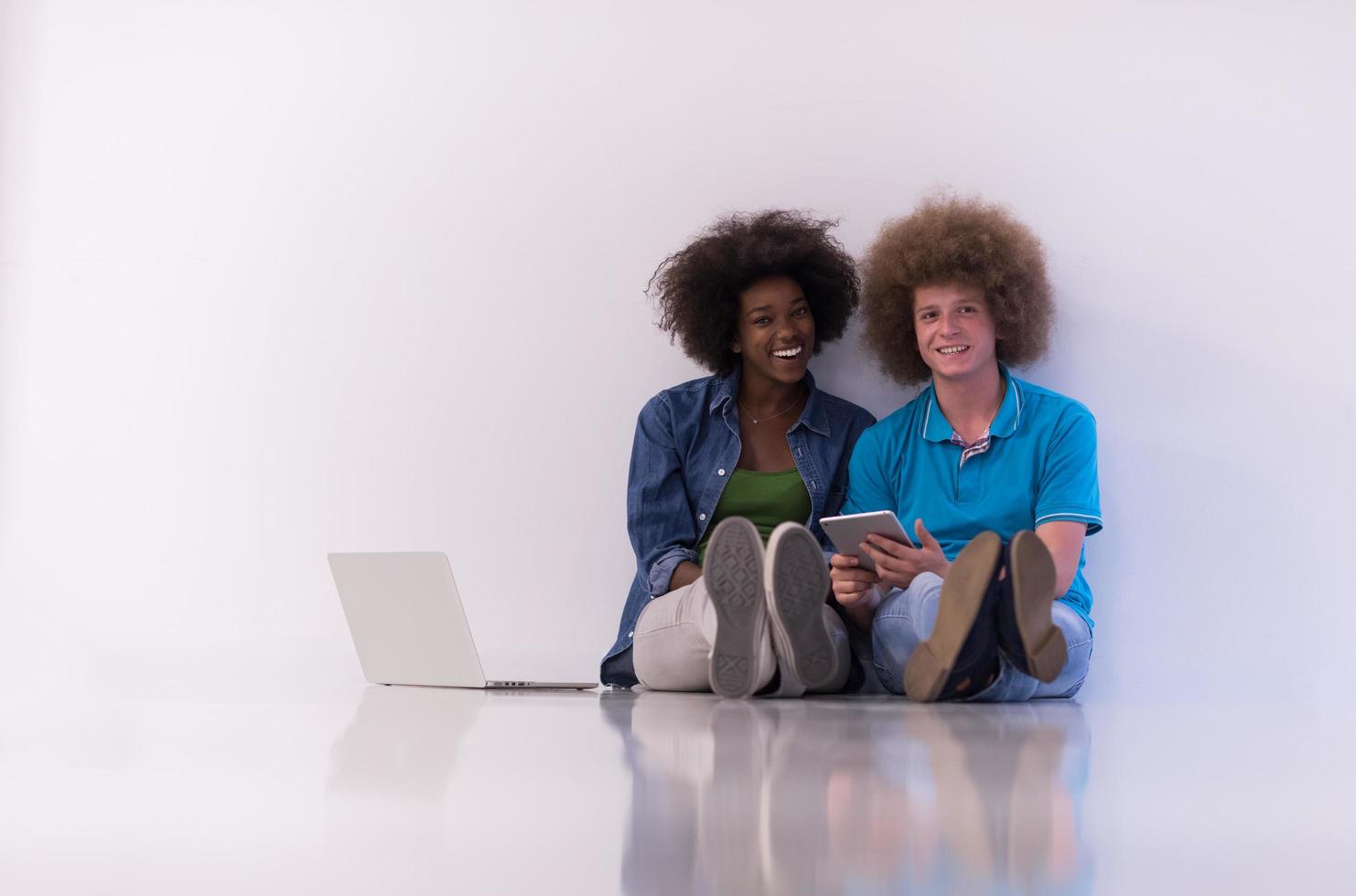 multiethnic couple sitting on the floor with a laptop and tablet photo