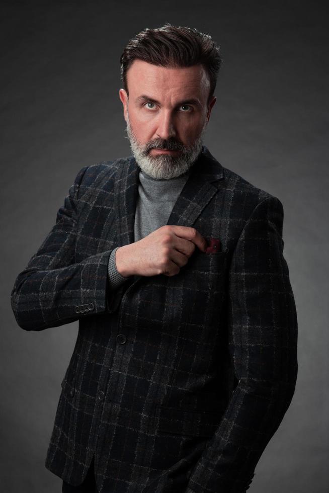 Portrait of a stylish elegant senior businessman with a beard and casual business clothes in photo studio isolated on dark background gesturing with hands