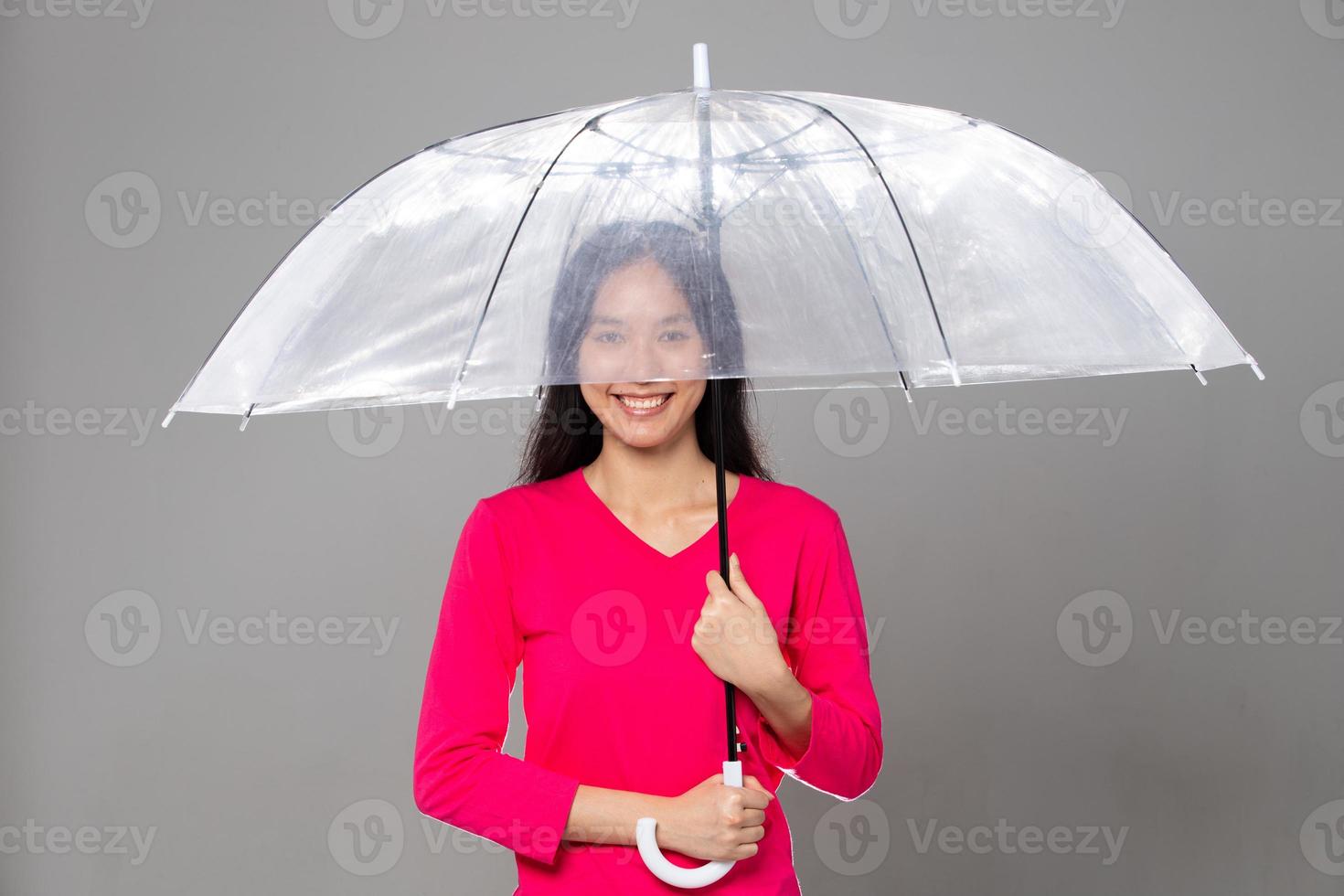 Asian young adult 20s Woman with long black straight hair wear pink dress. Female hold transparent umbrella, feeling emotion fashion happy smile, gray background isolated copy space photo