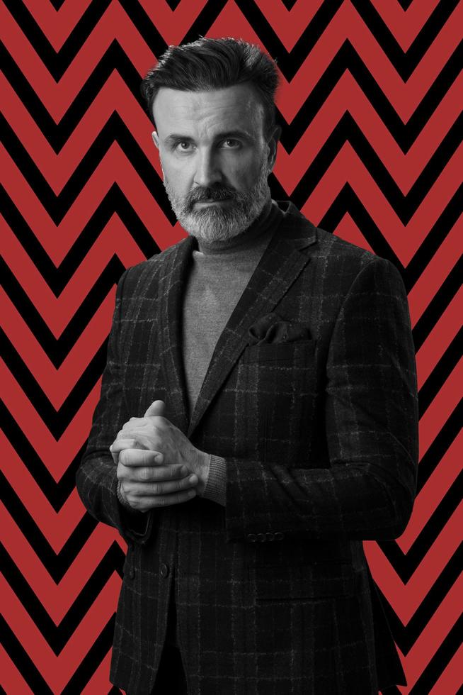 Black and white portrait of a stylish elegant senior businessman with a beard and casual business clothes against retro colorful pattern design background gesturing with hands photo