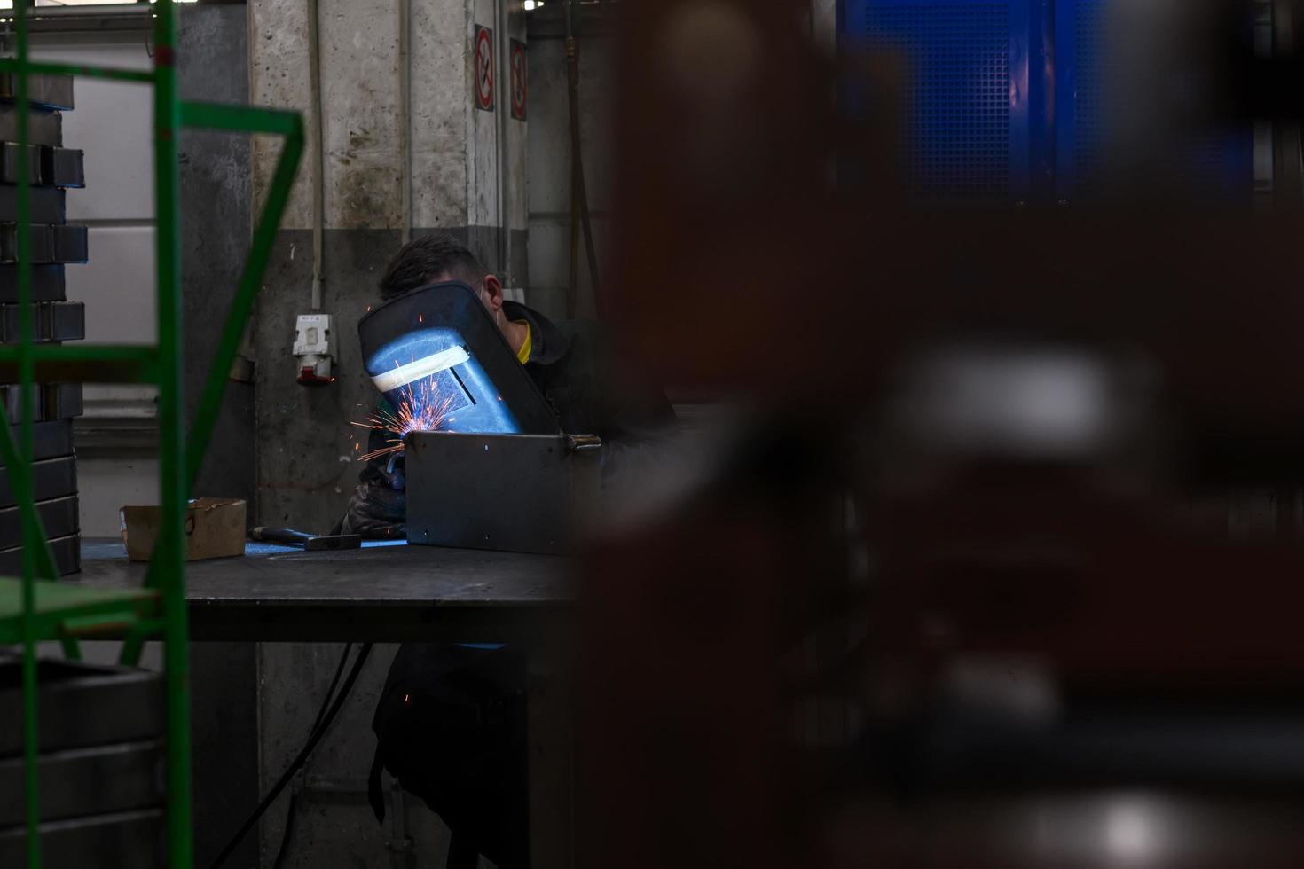 soldador profesional realiza trabajos con piezas metálicas en fábrica, chispas y electricidad. pancarta de trabajadores de la industria. foto