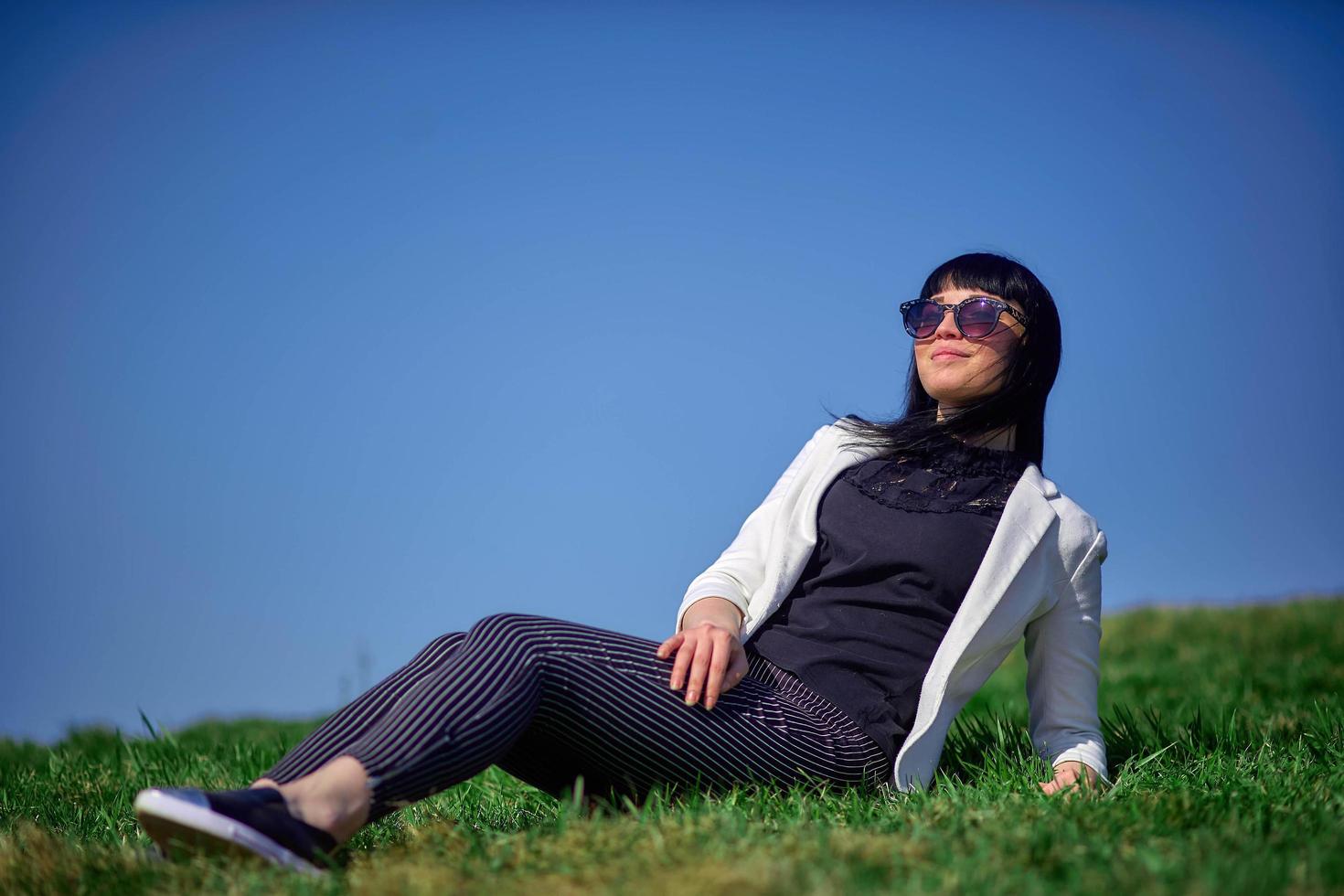Top view. beautiful young woman, lying in the grass, relaxing by a beautiful day in summer. She wears sunglasses photo