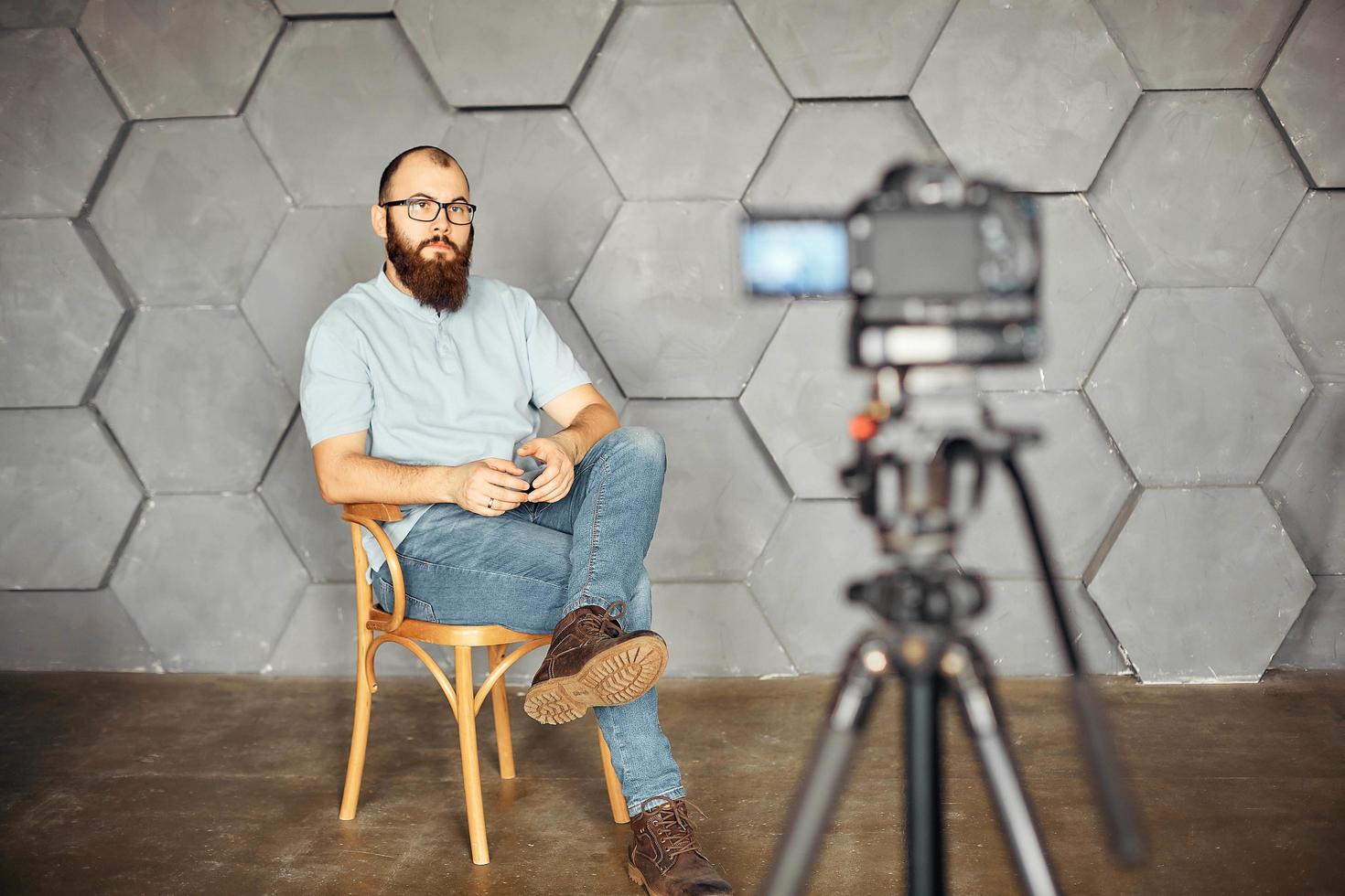 creación de contenidos para redes sociales. hombre barbudo filmando un video de sí mismo usando una cámara en un trípode. tecnología moderna y concepto de trabajo independiente de blogs. foto