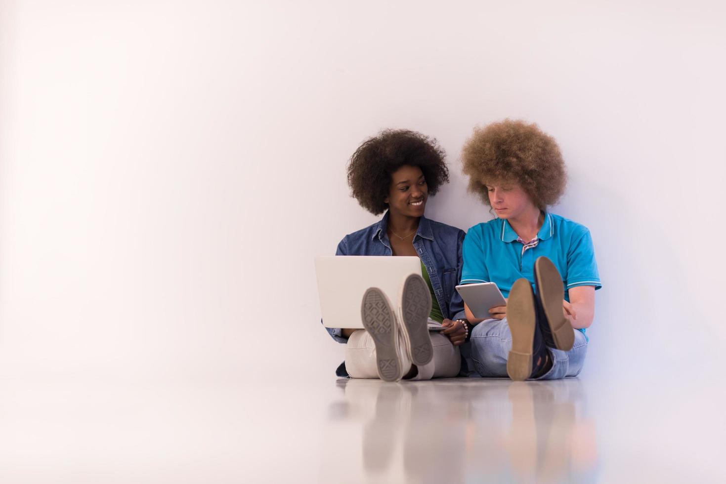 multiethnic couple sitting on the floor with a laptop and tablet photo