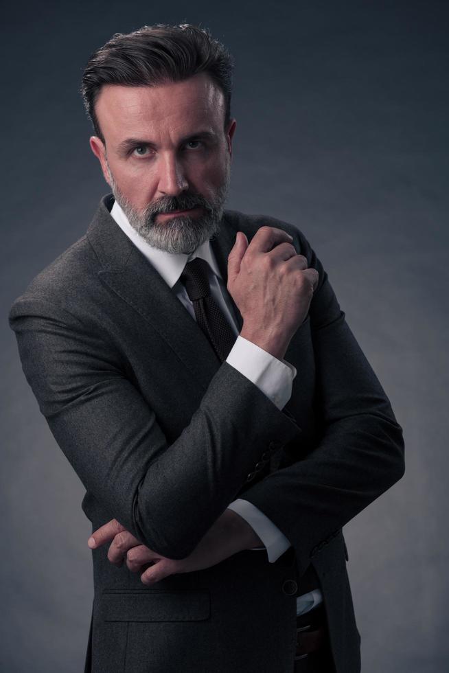 Portrait of a stylish elegant senior businessman with a beard and casual business clothes in photo studio isolated on dark background gesturing with hands