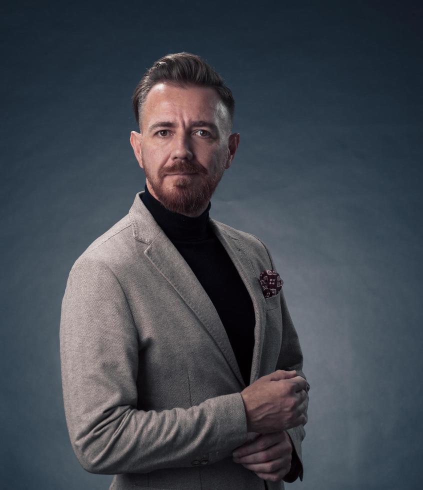 Portrait of a stylish elegant senior businessman with a beard and casual business clothes in photo studio isolated on dark background gesturing with hands