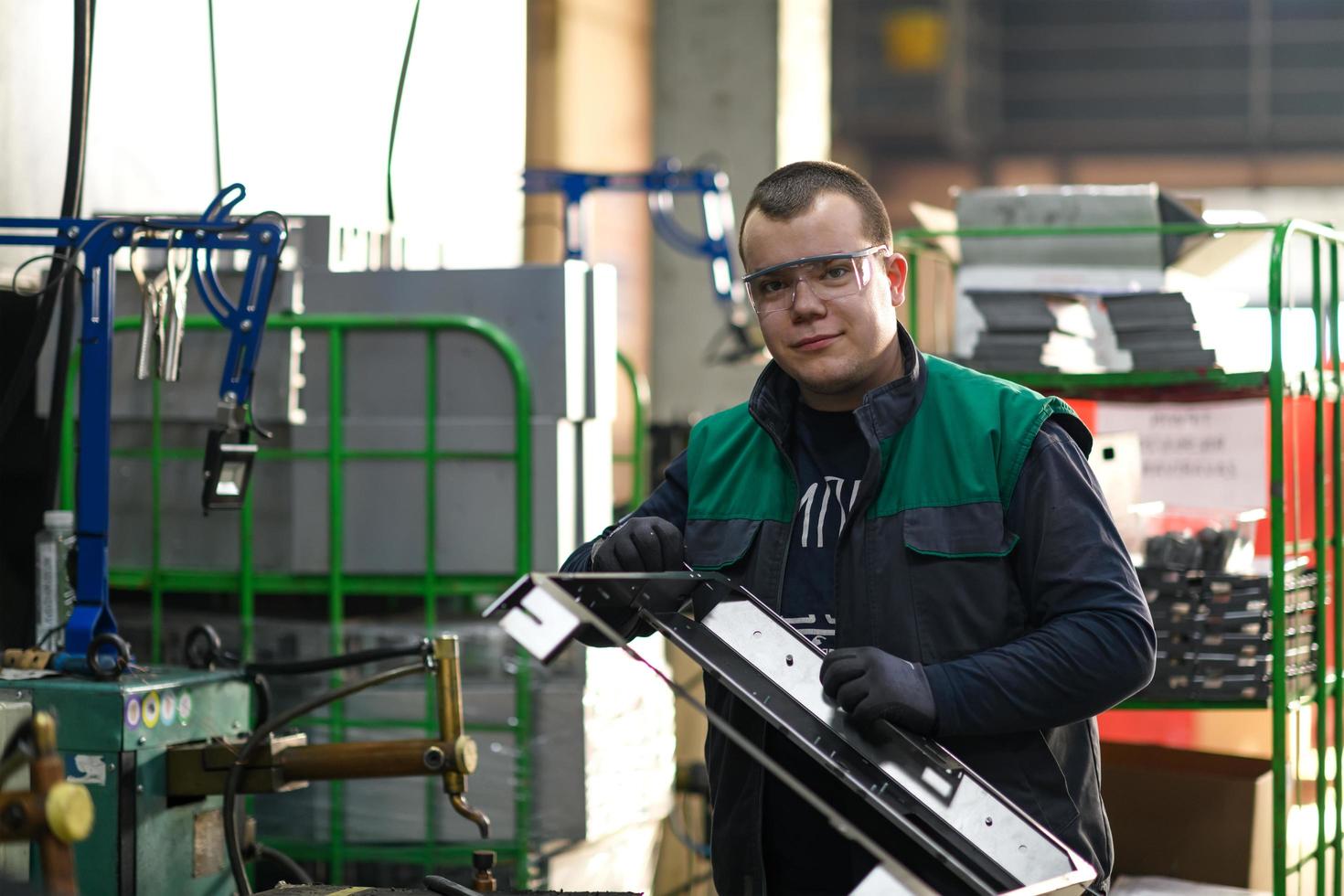 a uniformed worker working in a modern metal production and processing factory assembles parts of a new machine on his desk photo
