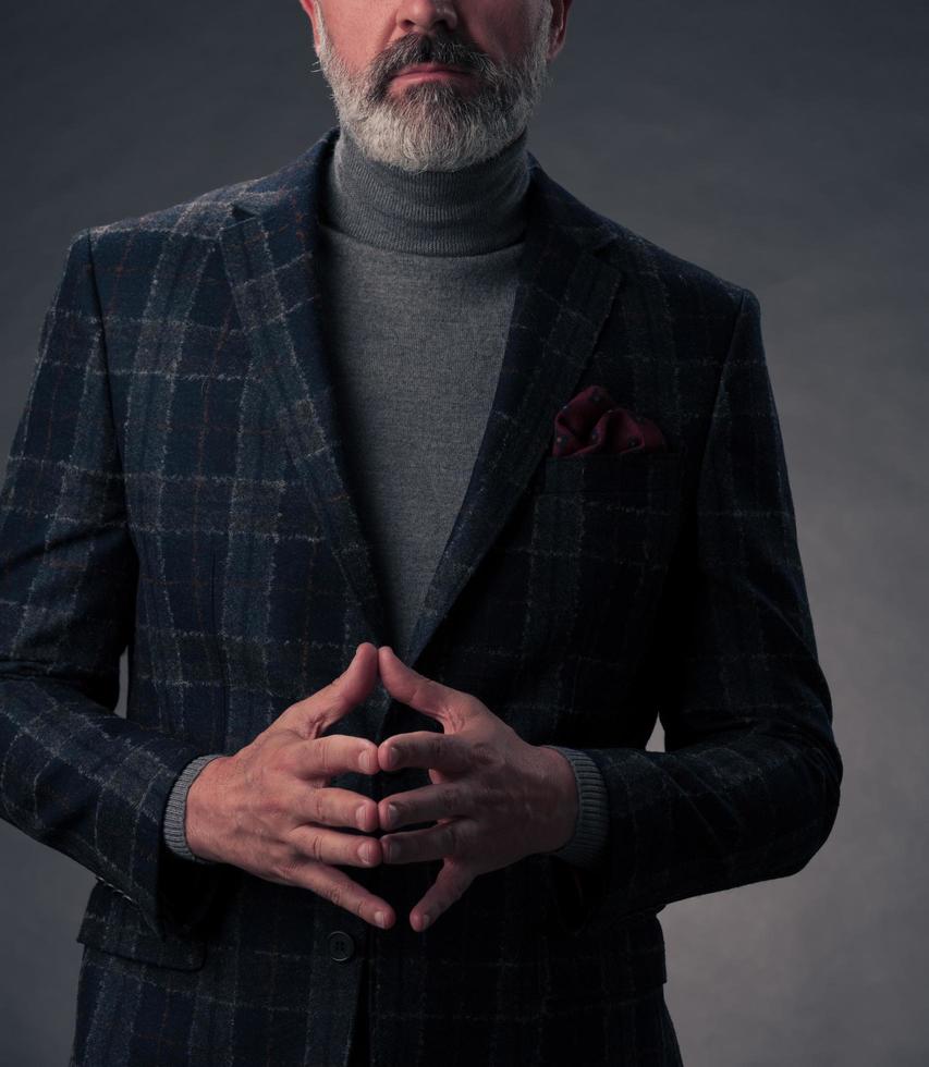 Portrait of a stylish elegant senior businessman with a beard and casual business clothes in photo studio isolated on dark background gesturing with hands