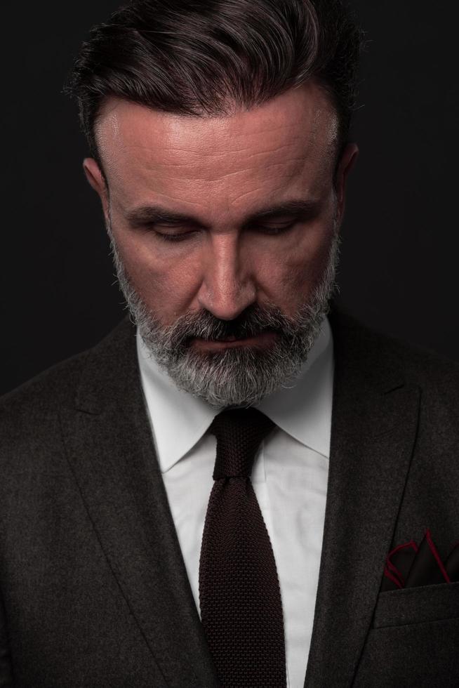 Portrait of a stylish elegant senior businessman with a beard and casual business clothes in photo studio isolated on dark background gesturing with hands