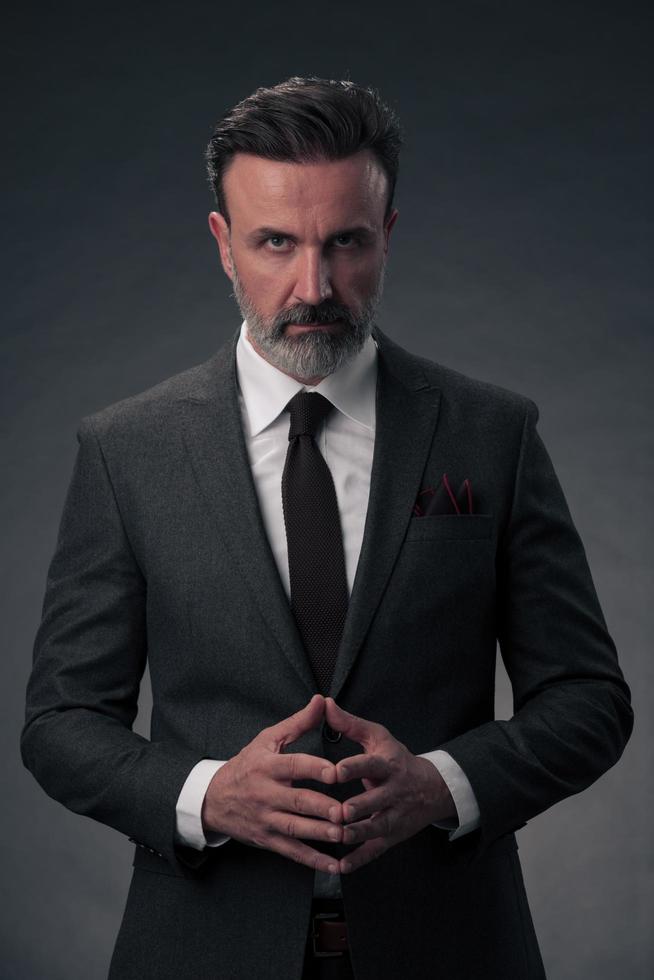 Portrait of a stylish elegant senior businessman with a beard and casual business clothes in photo studio isolated on dark background gesturing with hands