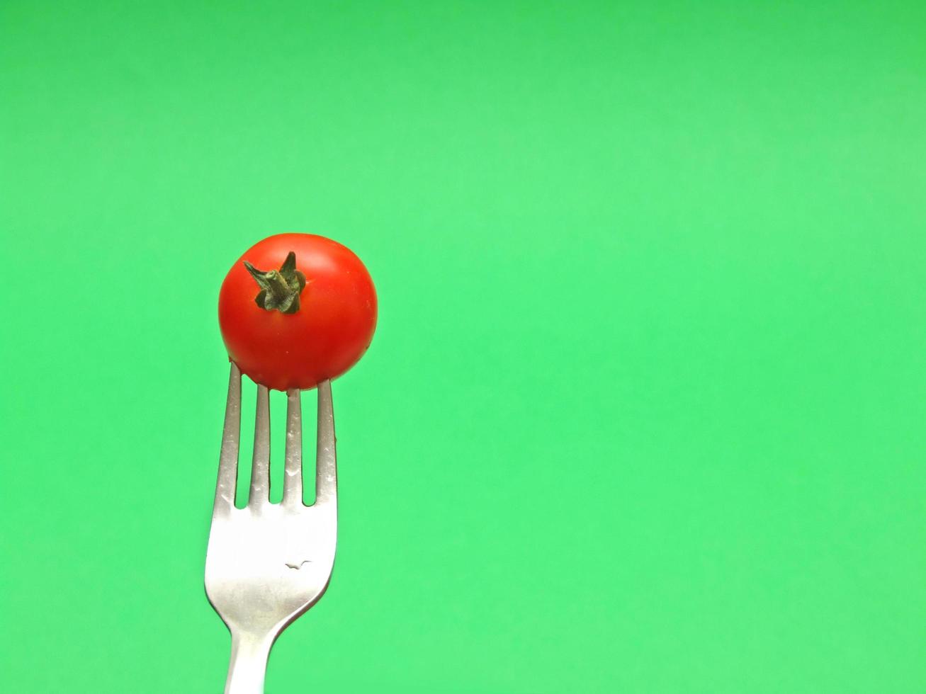 fresh tomato on fork with green background photo