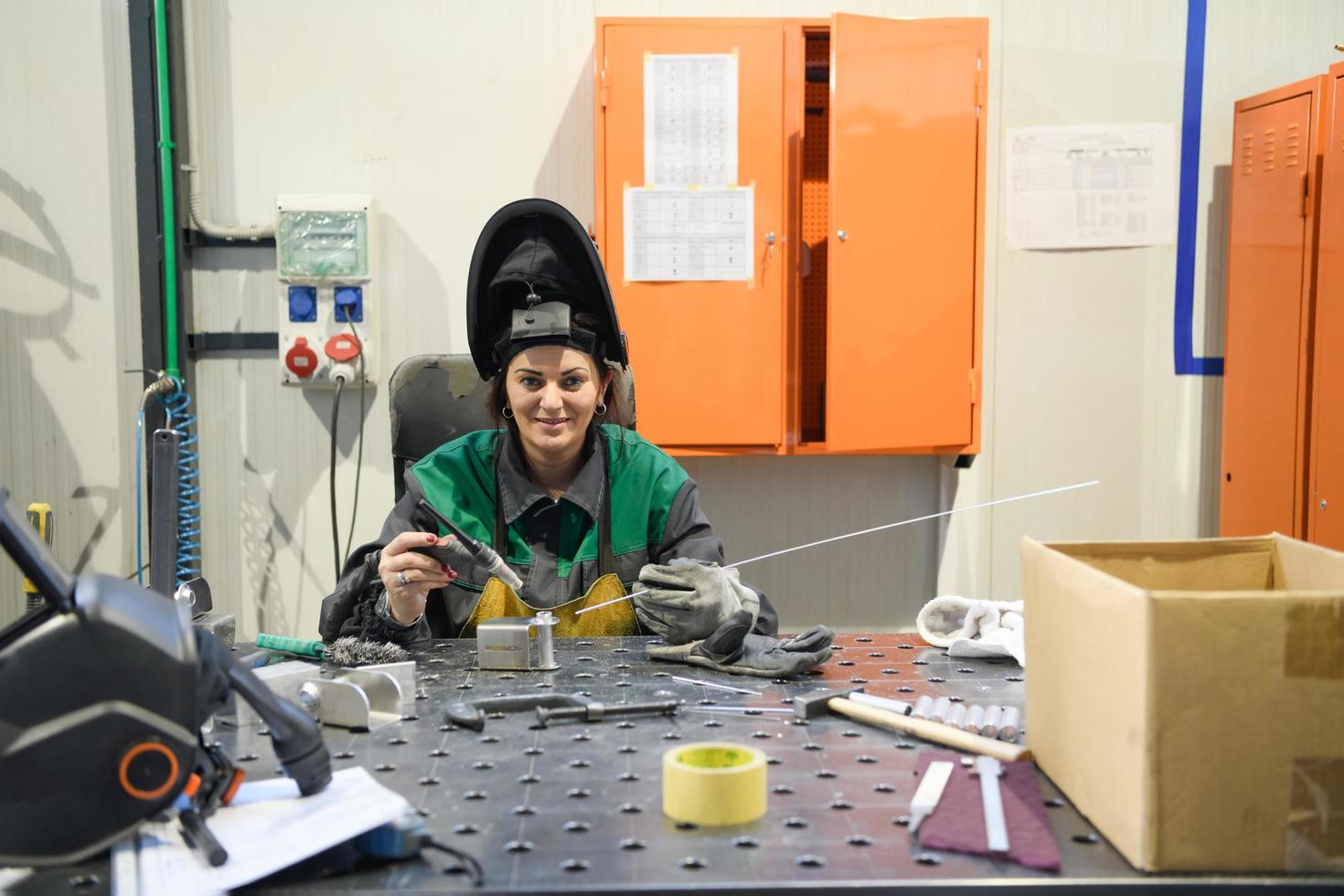 A woman employed in a modern factory for the production and processing of metals in a work uniform welds metal materials photo