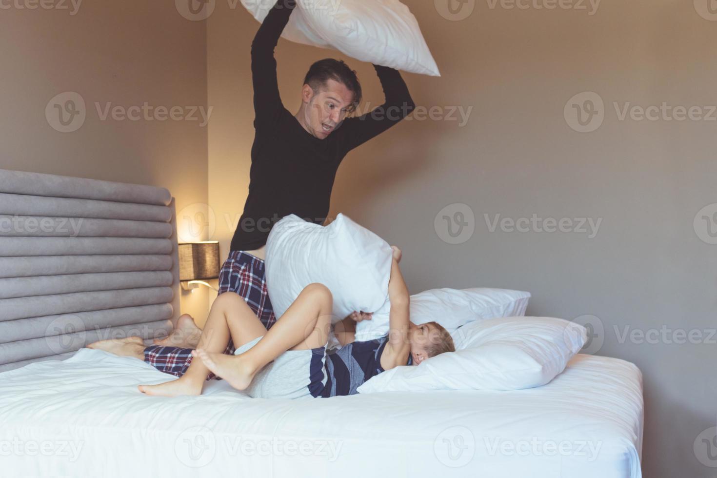 Playful father and son fighting with pillows on the bed. photo