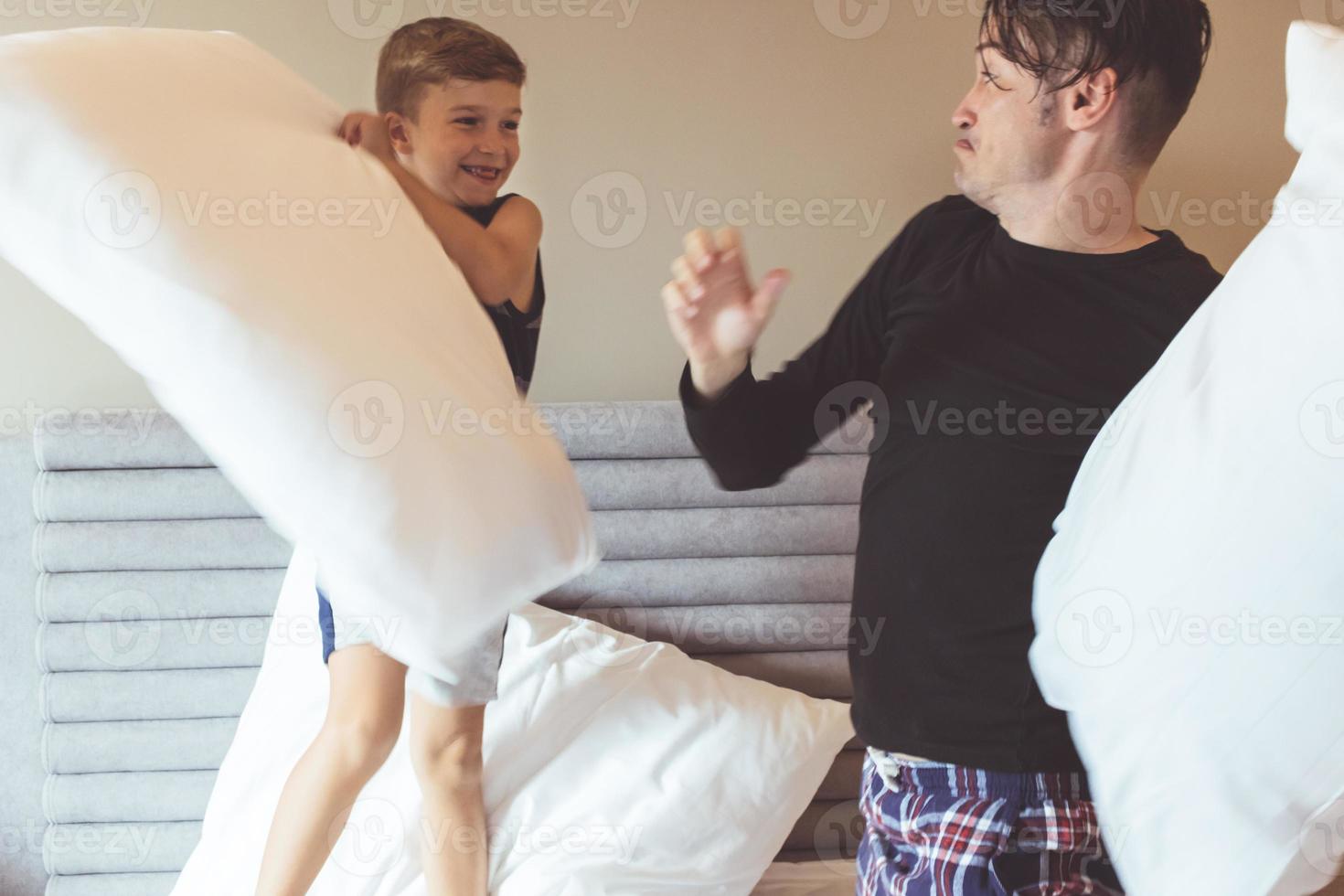 Happy boy and his father pillow fighting in the bedroom. photo