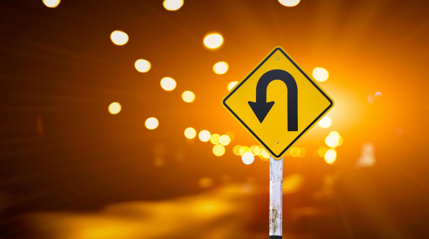 Left u-turn sign on pole, streetlights bokeh background. Concept for traffic sign at night. photo