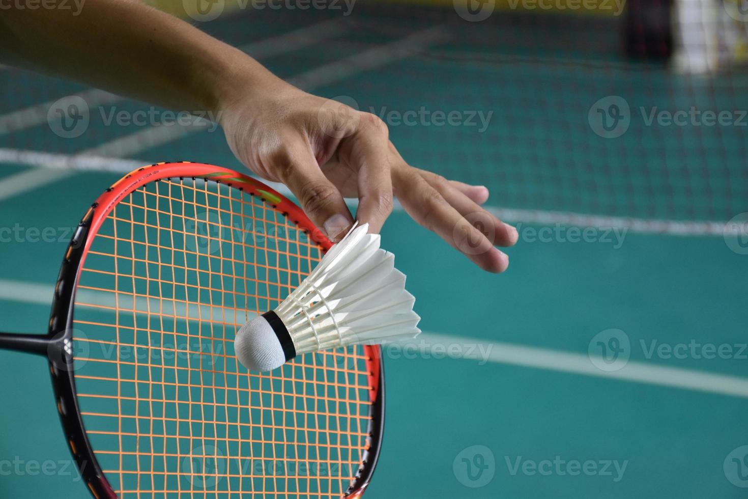Badminton player holds racket and white cream shuttlecock in front of the net before serving it to another side of the court. photo