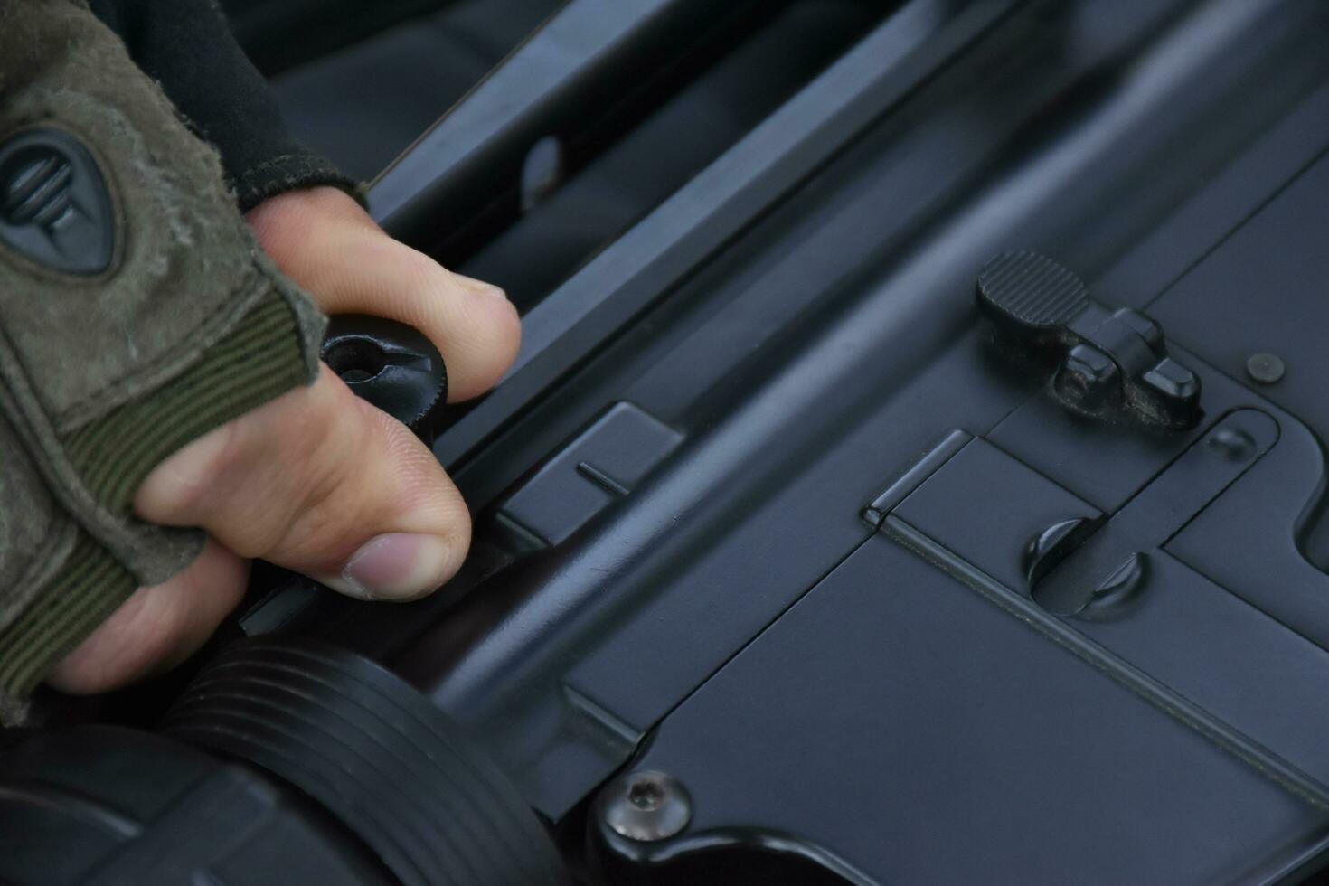 Ammunition rail of automatic black airsoft gun or BBGUN was checking by gunman. Selective focus on hand, shooting sports and security training concept. photo