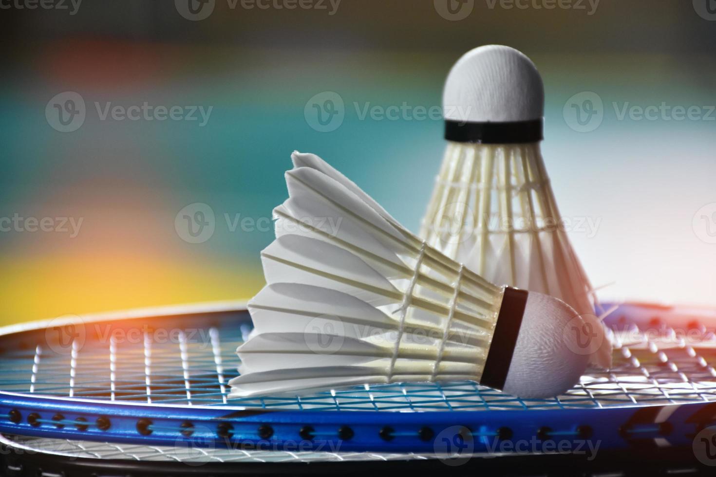 Cream white badminton shuttlecock and racket with neon light shading on green floor in indoor badminton court, blurred badminton background, copy space. photo