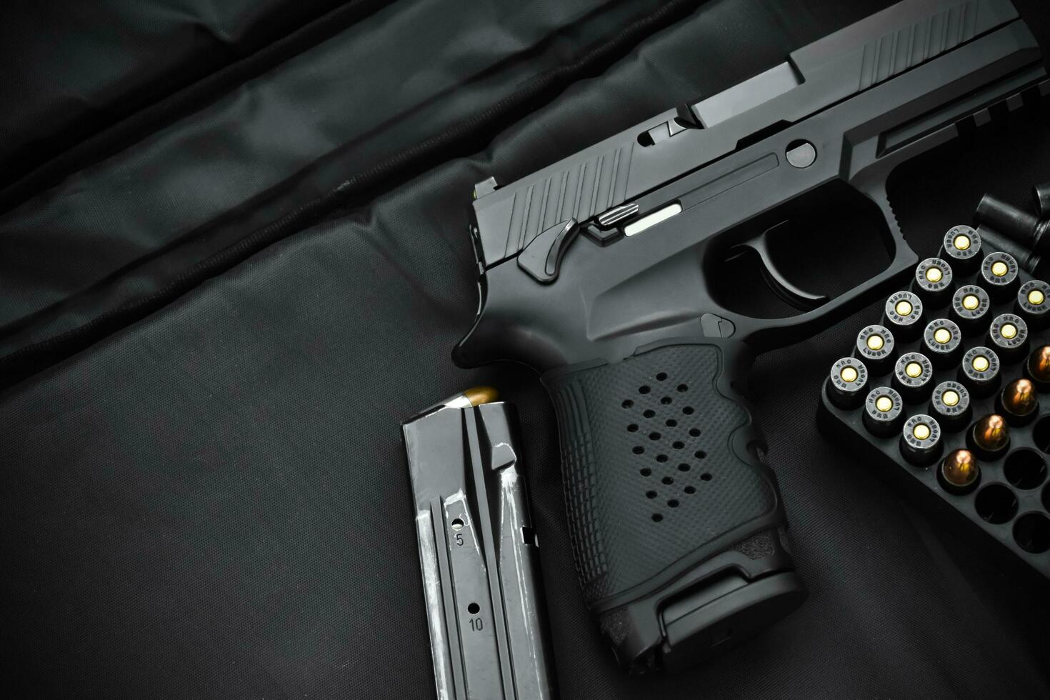 Automatic black 9mm pistol and bullets on black leather background, selective and soft focus. photo