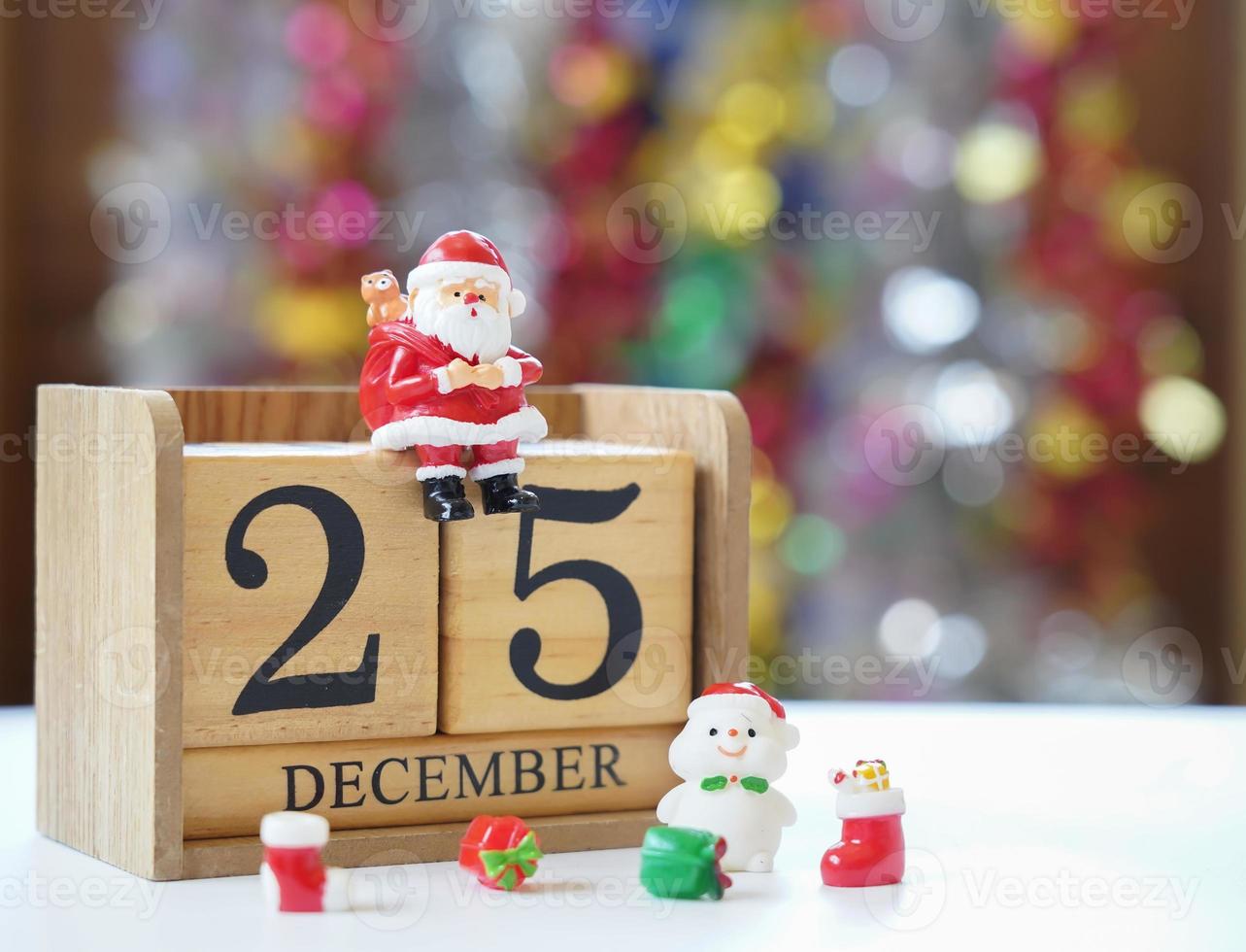 Papá Noel sentado en un bloque de madera con fecha del 25 de diciembre con muñecos de nieve y regalos esperando un divertido festival de Navidad y feliz año nuevo para hacer una tarjeta de felicitación. foto