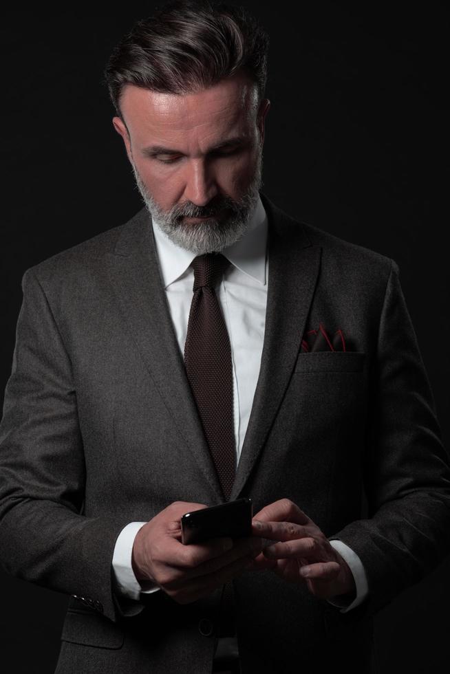 Portrait of adult businessman wearing trendy suit and sitting in modern studio on stylish chair against the black background photo