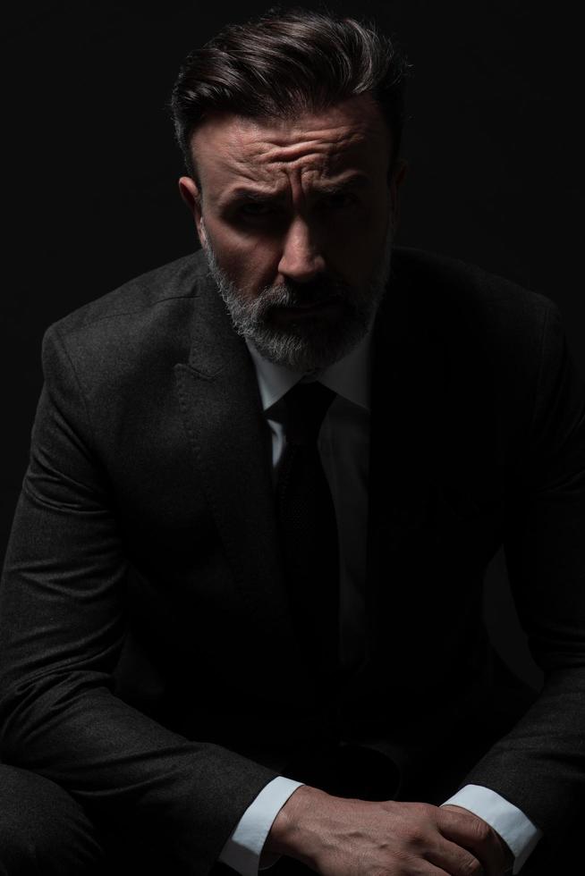 Portrait of a stylish elegant senior businessman with a beard and casual business clothes in photo studio isolated on dark background gesturing with hands