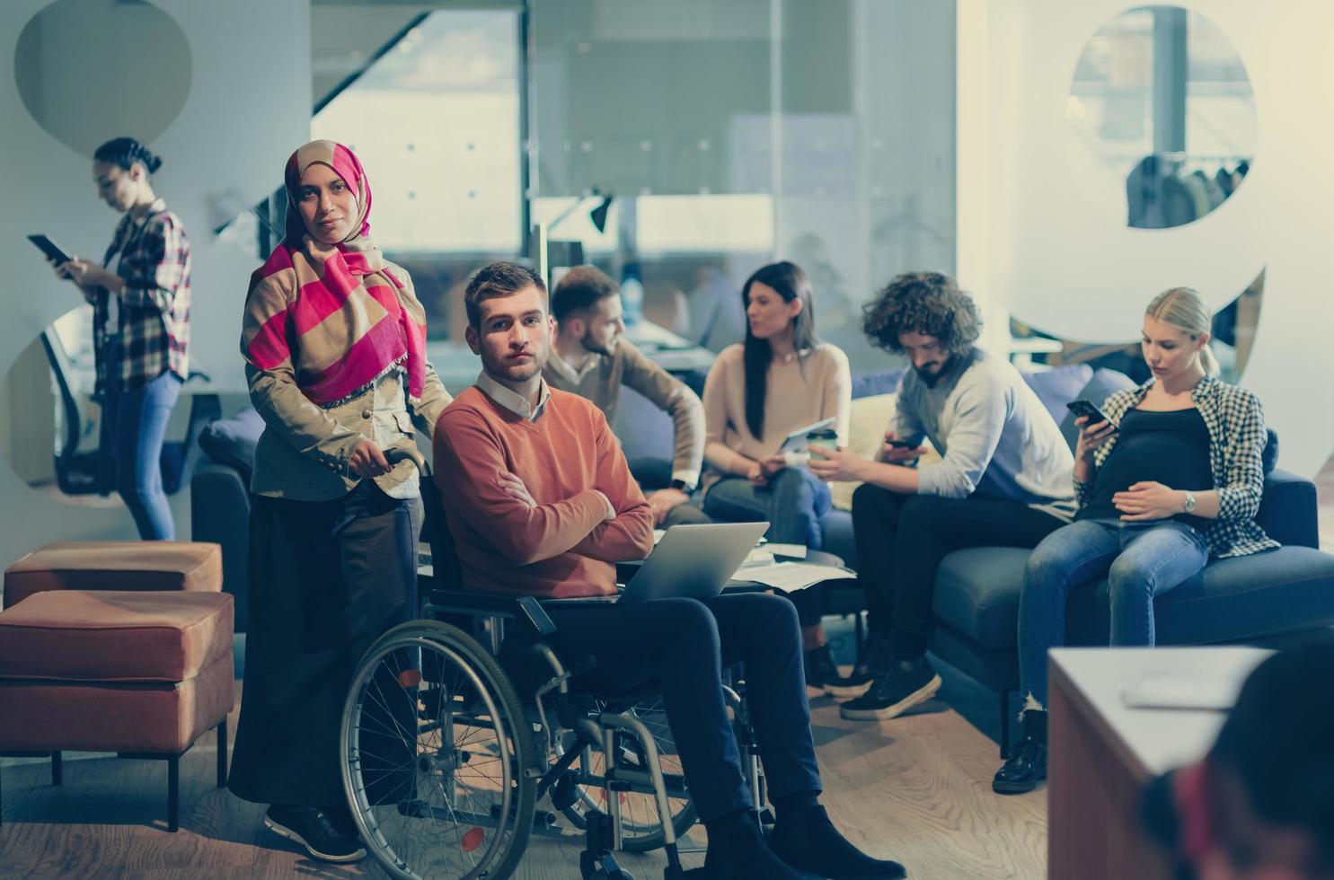 Disabled businessman in a wheelchair at work in modern open space coworking office with team photo