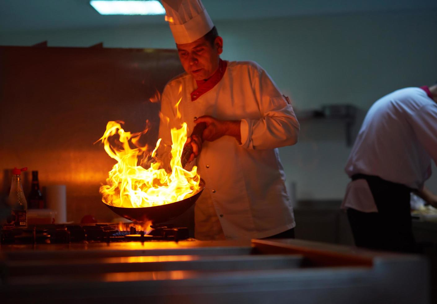 chef en la cocina del hotel prepara comida con fuego foto