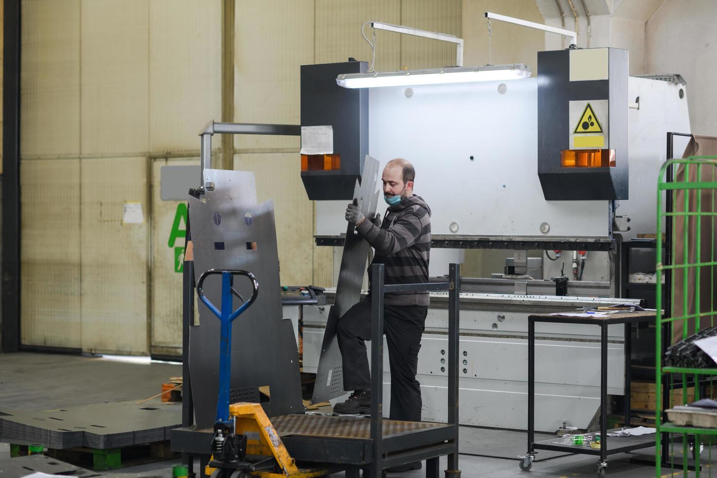 Turkey, 2022 - a worker working in a modern industry prepares material for processing on a cnc machine, wears a protective mask on his face due to a coronary virus pandemic photo