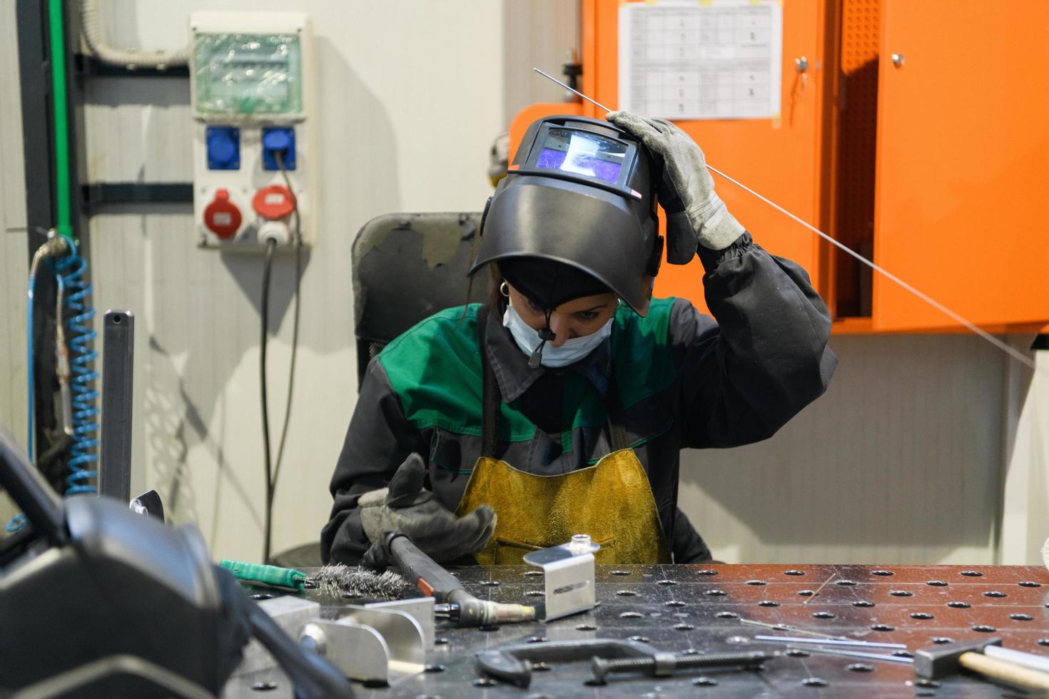 una mujer empleada en una fábrica moderna para la producción y procesamiento de metales en un uniforme de trabajo suelda materiales metálicos foto