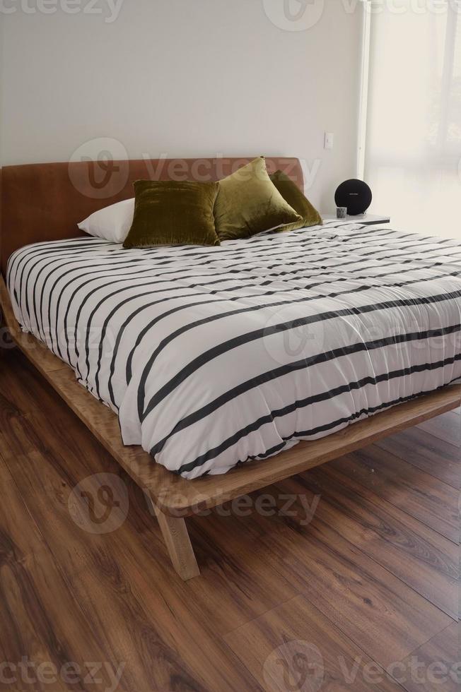 somier, dormitorio con tapete en el piso, cazuela de barro al fondo, credenza de madera y espejo. foto