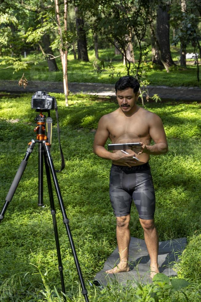 Active handsome male yogi drawing tablet strolling forest before or after a workout. Young hispanic athletic man yoga class with a fitness mat photo