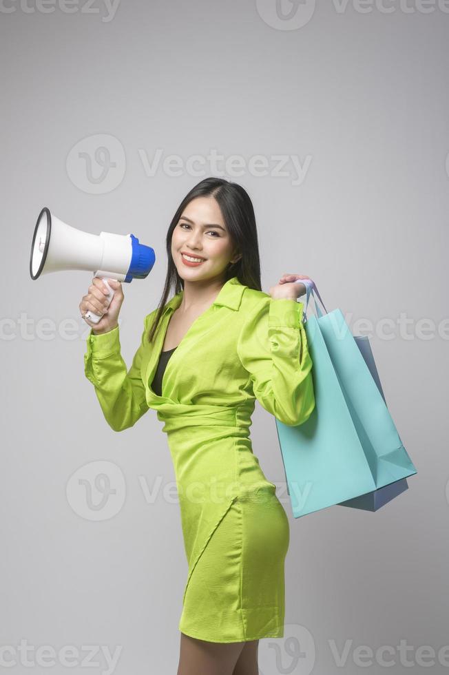 Beautiful woman holding megaphone and shopping bag over white background studio, shopping and finance concept. photo