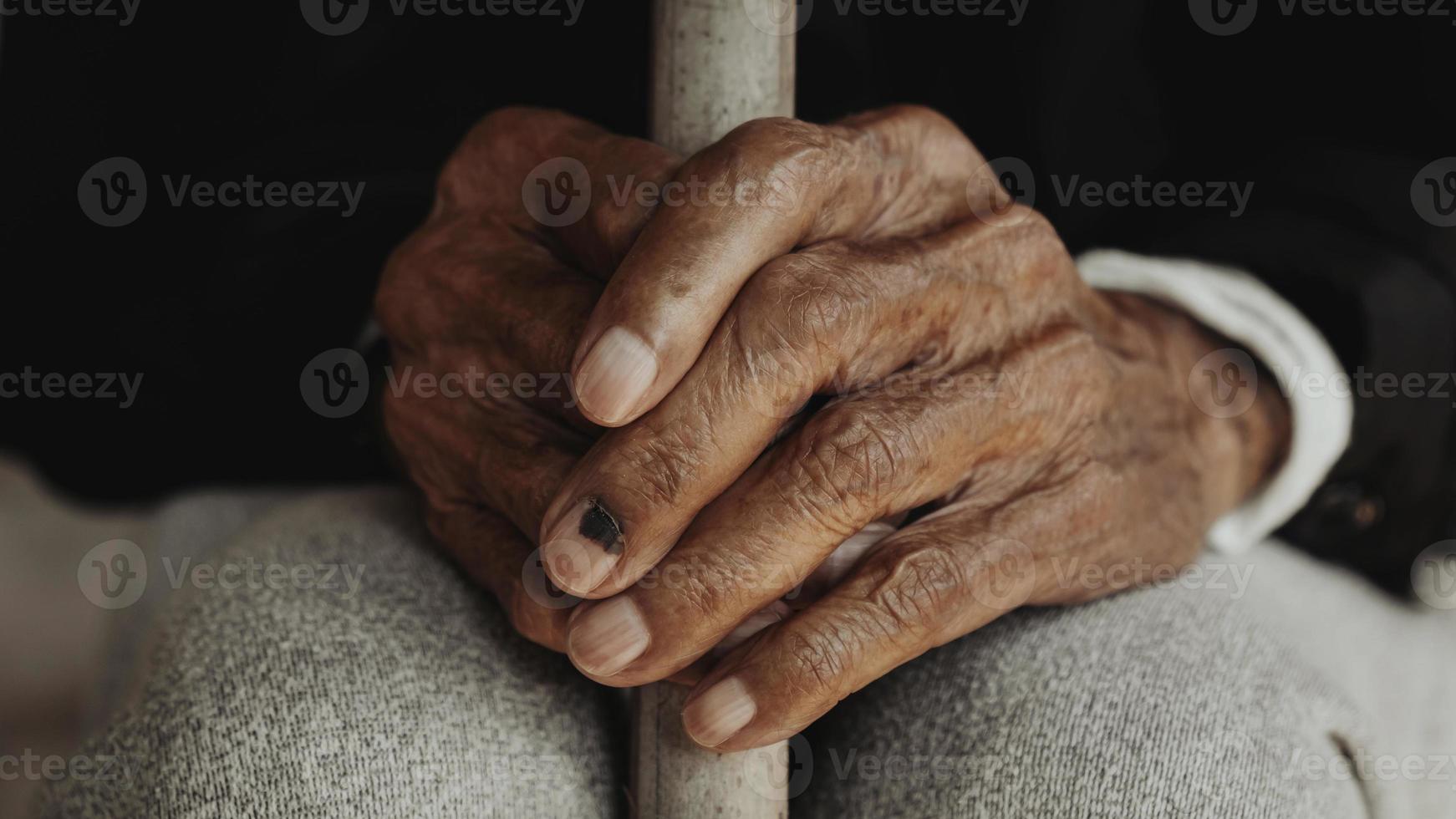 Asian old man sitting with his hands on a walking stick. photo