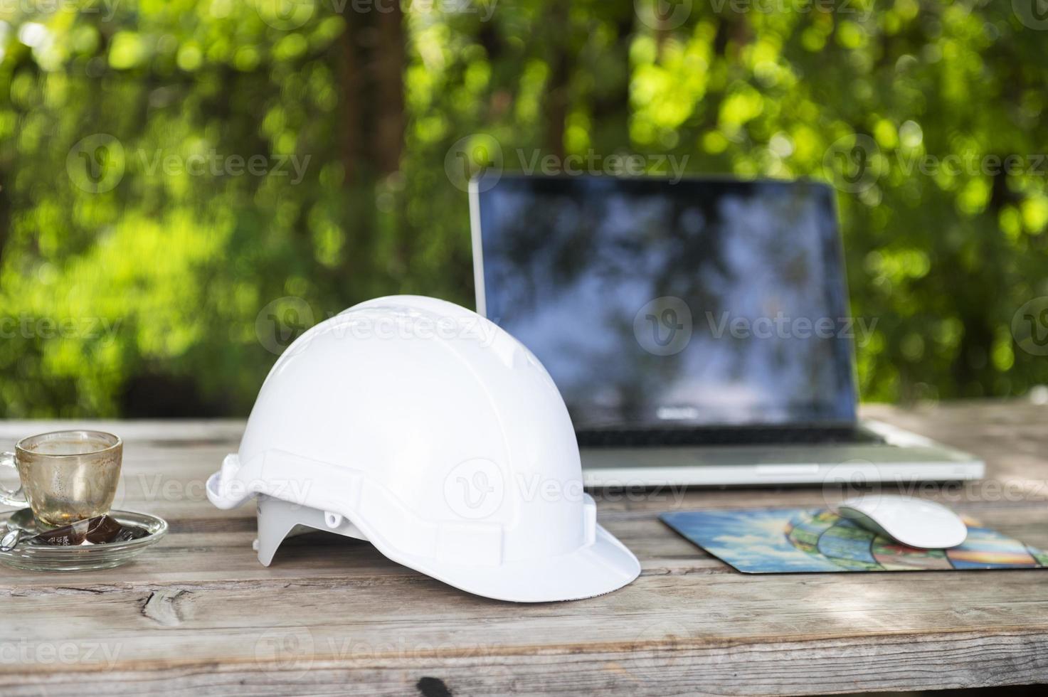 White helmet and computer at cafe with sunlight background, engineer view sitting construction planning photo