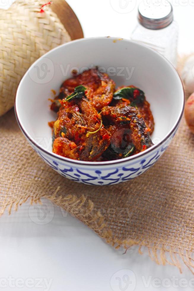 Spicy Stir Fried Catfish served in a Thai style patterned bowl on a white table. photo