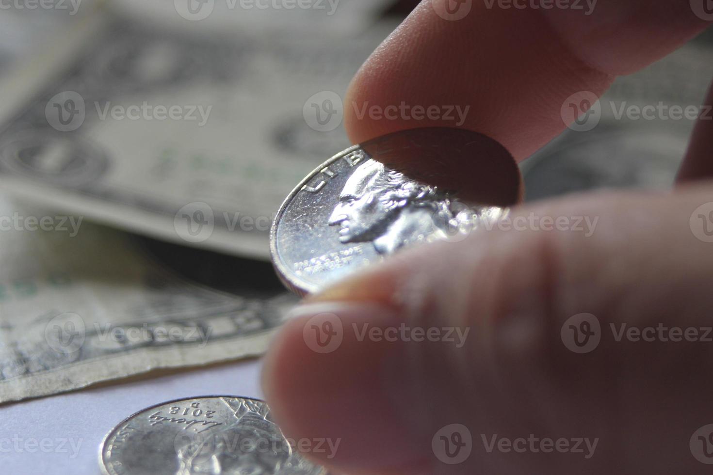 Man's hand picking up a quarter coin from a pile of banknotes and coins. photo