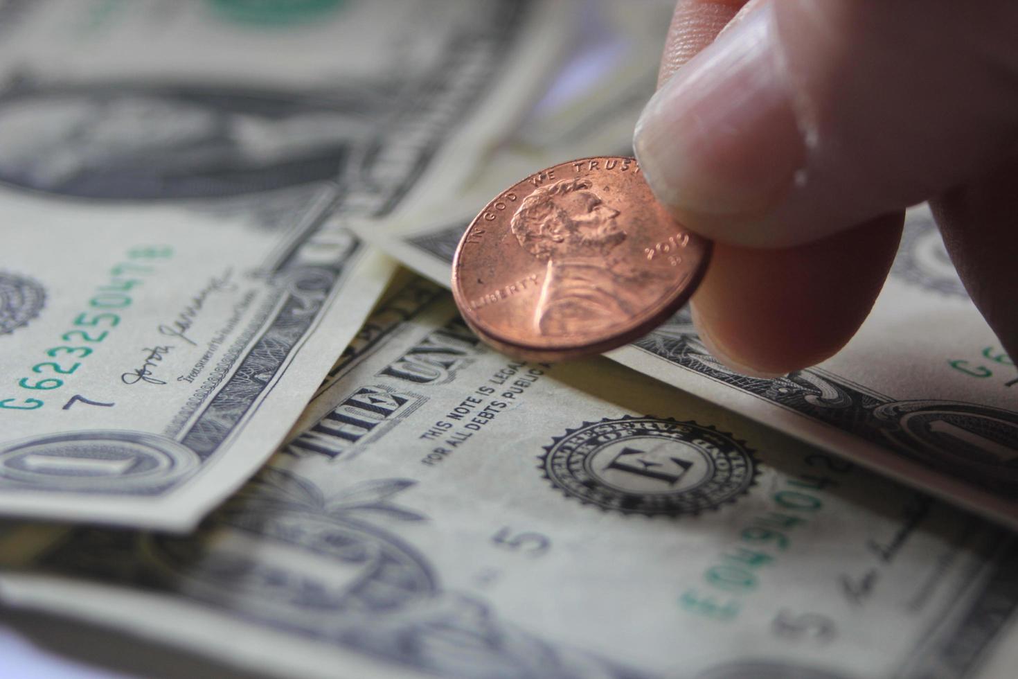 Man's hand picking up penny or cent coin from a pile of banknotes and coins. photo