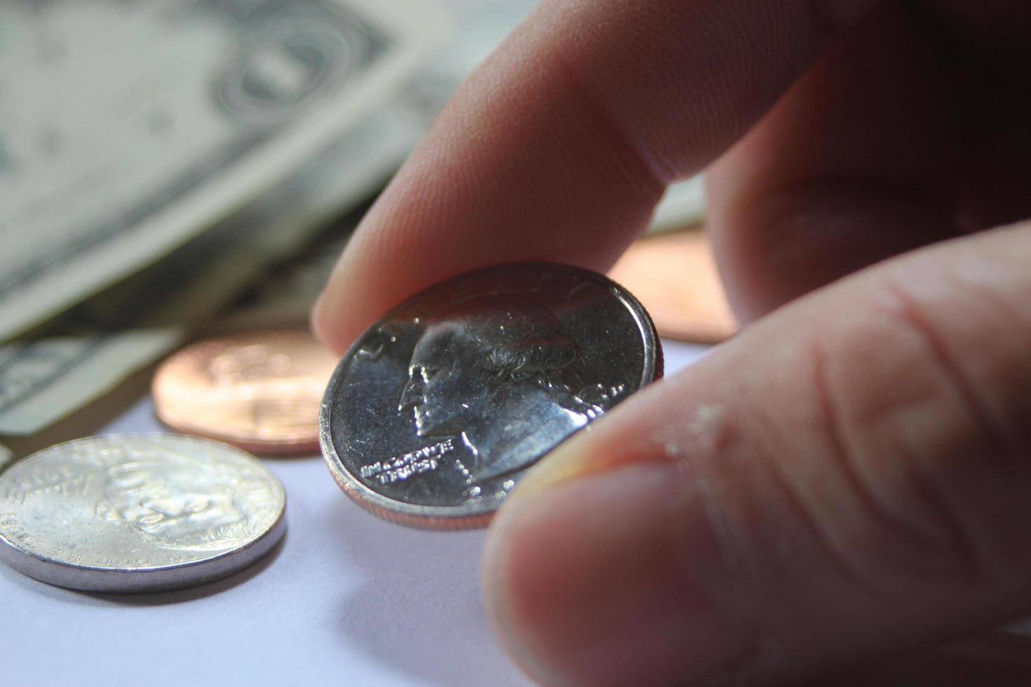 Man's hand picking up a quarter coin from a pile of banknotes and coins. photo