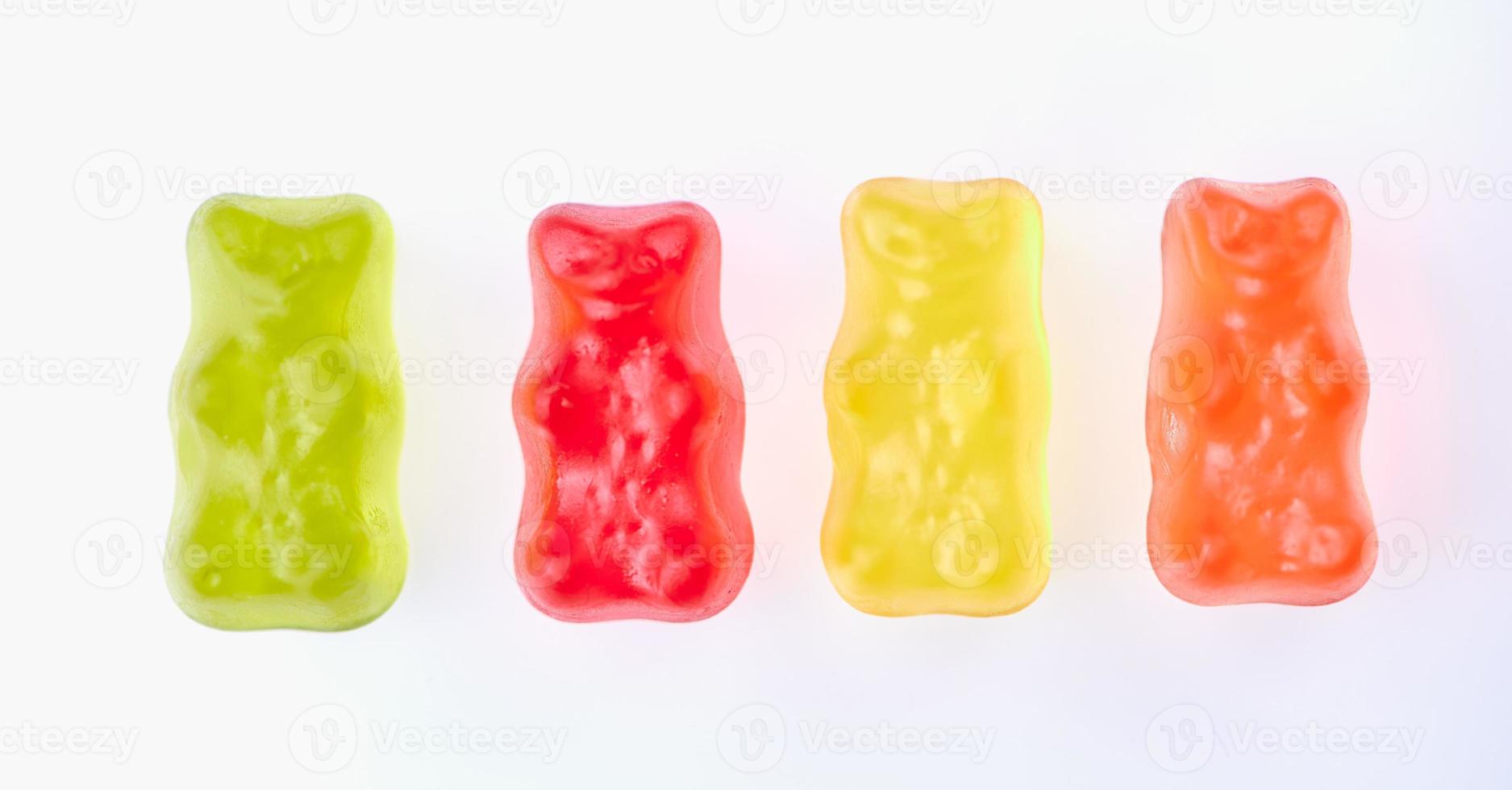 green, red, yellow and orange colored gummy bears in a row side by side on white background photo