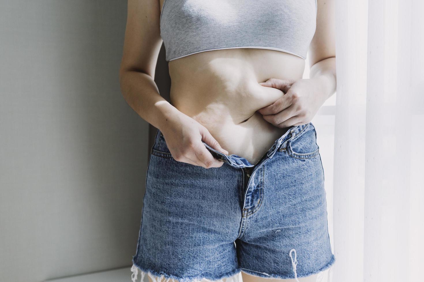 hermosa mujer gorda con cinta métrica usa su mano para exprimir el exceso de grasa que está aislado en un fondo blanco. ella quiere perder peso, el concepto de cirugía y descomponer grasa bajo el foto