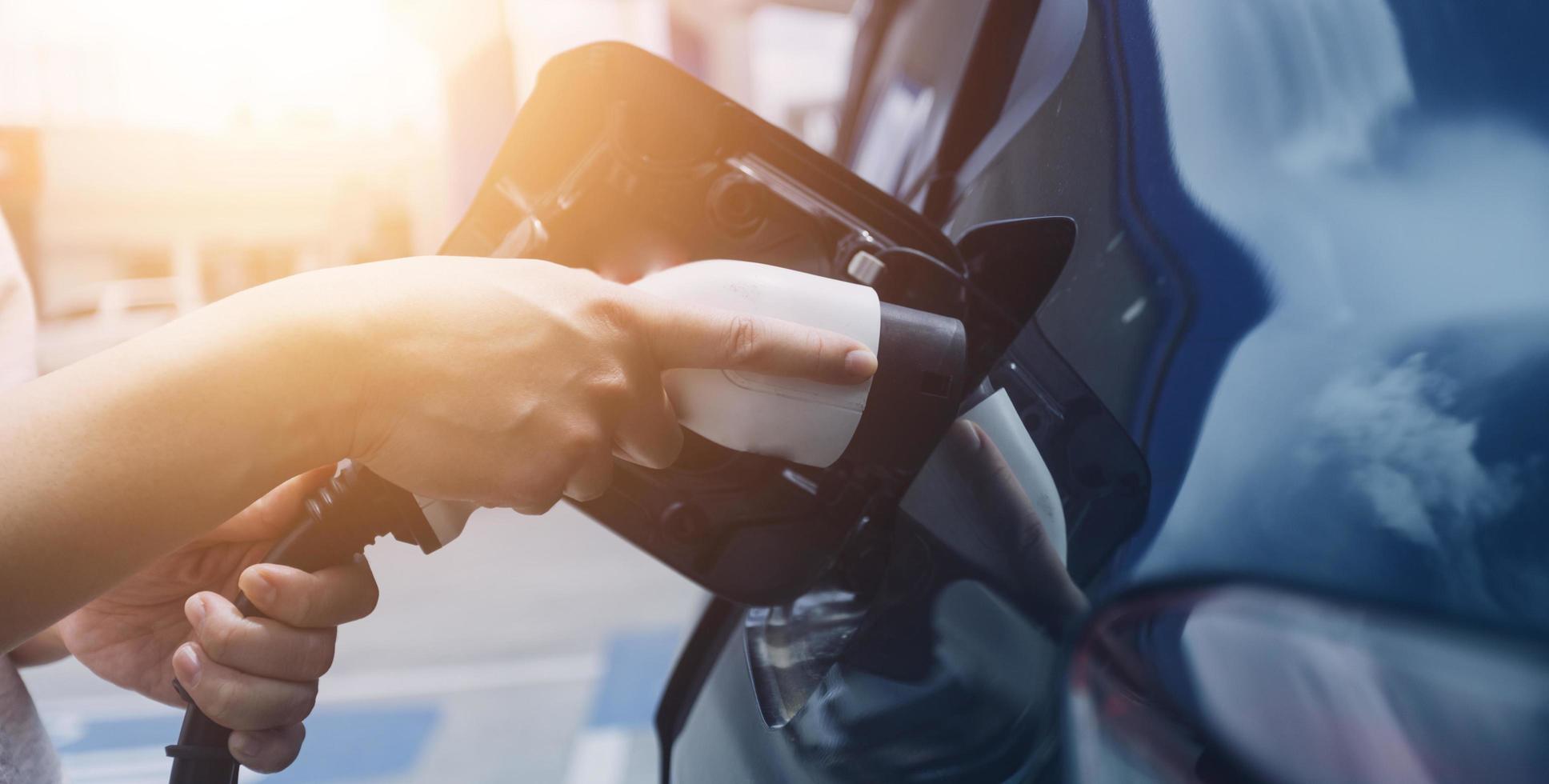 Hand plugging in a charger in an electric car socket.Electric car or ev is charging at station photo