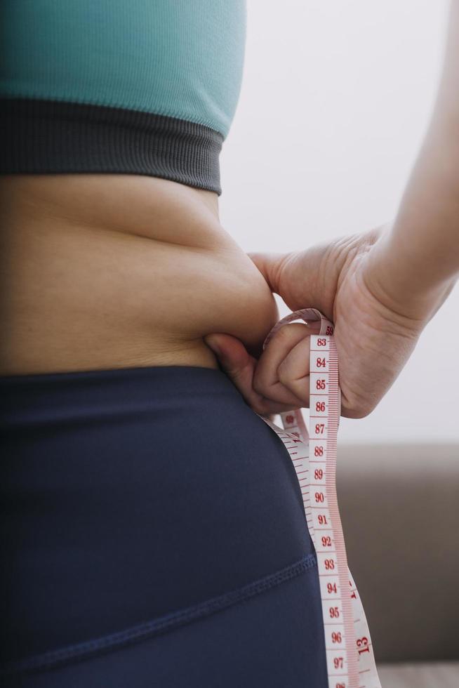 hermosa mujer gorda con cinta métrica usa su mano para exprimir el exceso de grasa que está aislado en un fondo blanco. ella quiere perder peso, el concepto de cirugía y descomponer grasa bajo el foto