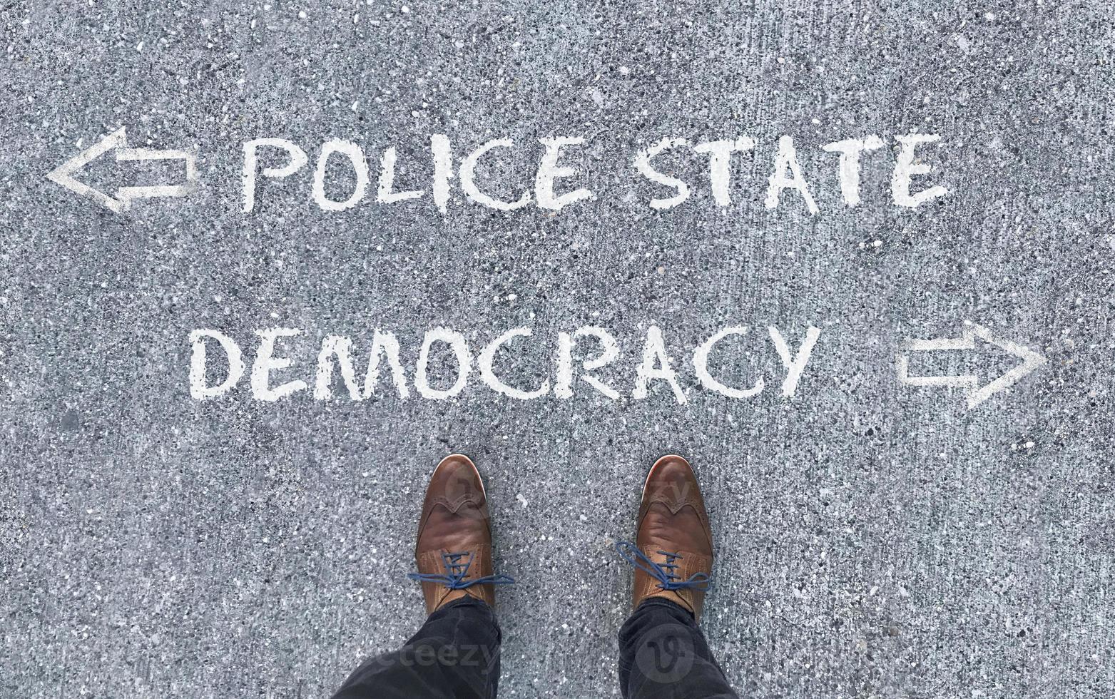 vista superior de un hombre parado frente a las palabras estado policial y democracia con flechas apuntando hacia el lado izquierdo y derecho de la imagen foto