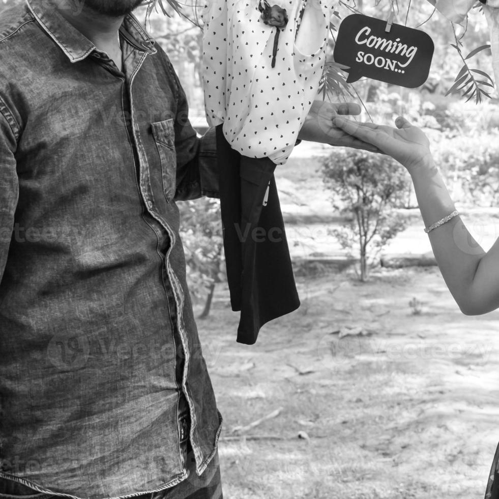 Indian couple posing for maternity baby shoot. The couple is posing in a lawn with green grass and the woman is falunting her baby bump in Lodhi Garden in New Delhi, India - Black and White photo