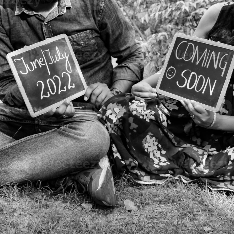 Indian couple posing for maternity baby shoot. The couple is posing in a lawn with green grass and the woman is falunting her baby bump in Lodhi Garden in New Delhi, India - Black and White photo